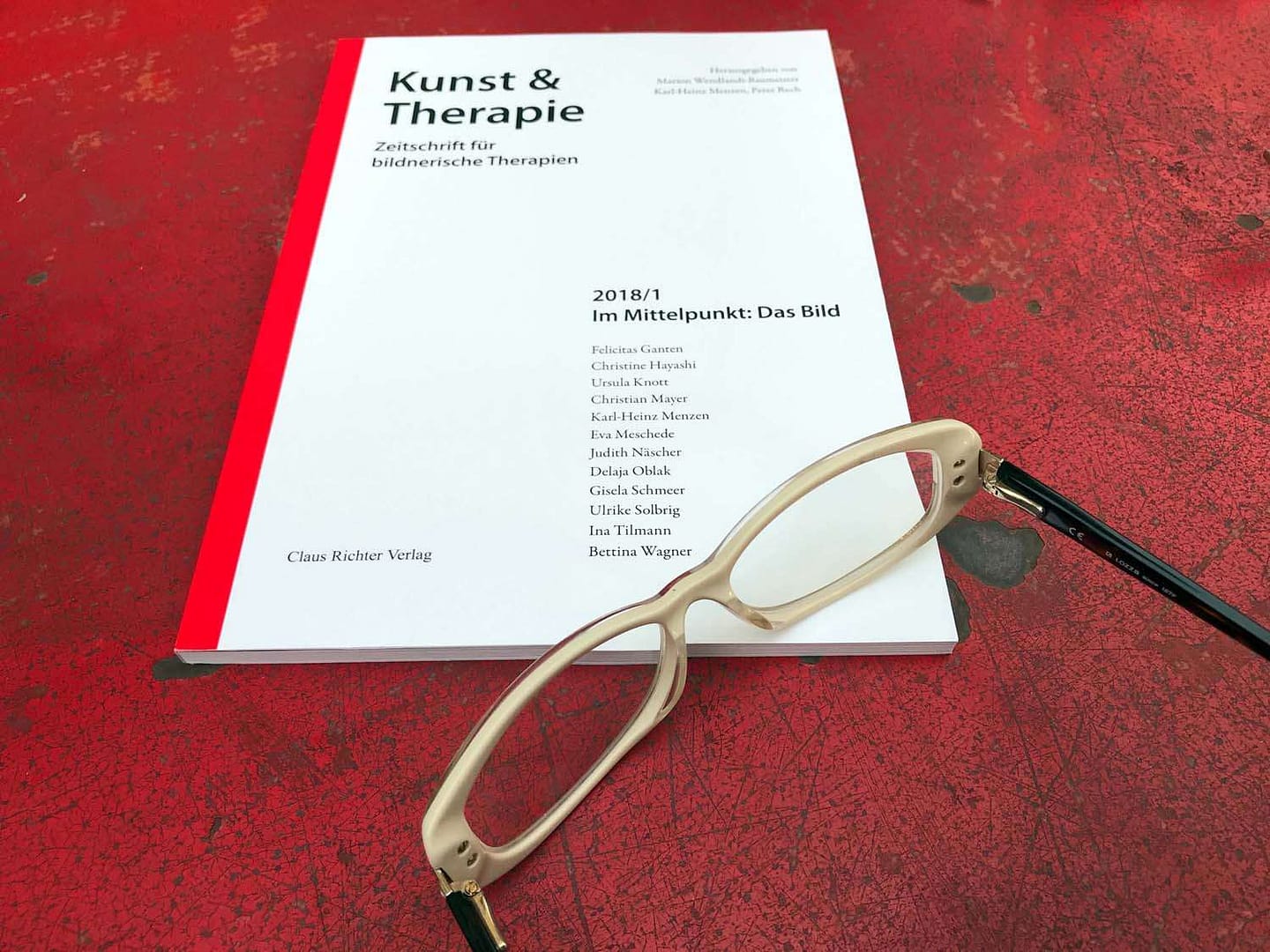 Ein Magazin mit dem Titel 'Kunst & Therapie' liegt auf einem roten Tisch mit einer Brille daneben. Es handelt sich um die Ausgabe 2018/1 zum Thema 'Im Mittelpunkt: Das Bild'.