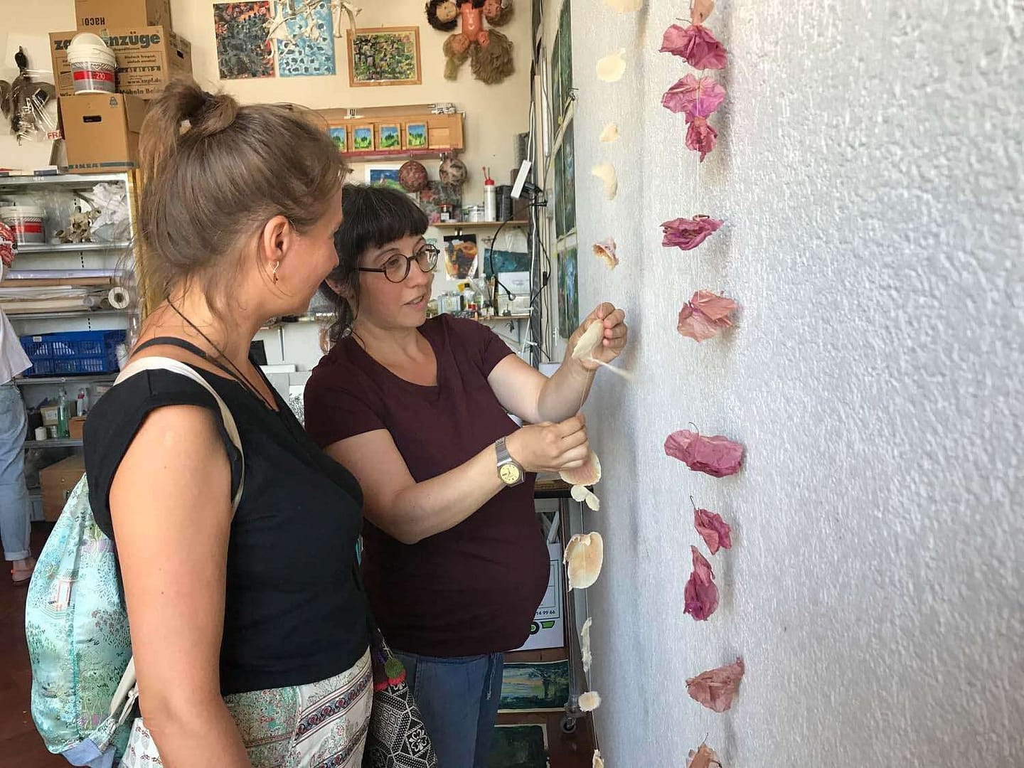 Zwei Frauen in einem kreativen Atelier, die an einer Wand mit dekorativen Blüten arbeiten.
