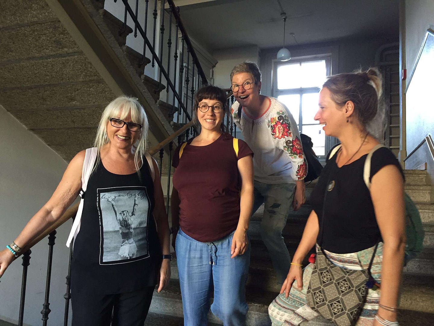 Vier Frauen lächeln und stehen auf einer Treppe in einem Gebäude.