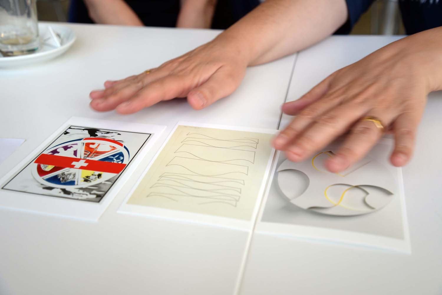 Eine Person berührt drei verschiedene Karten auf einem Tisch, die unterschiedliche grafische Designs zeigen.