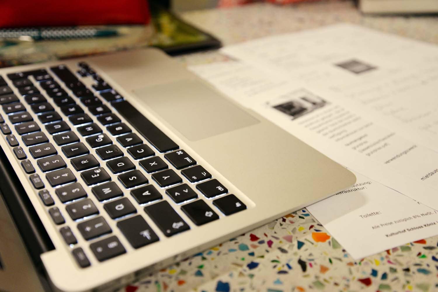 Nahaufnahme einer Laptop-Tastatur mit einem Blatt Papier auf einem bunten Tisch.