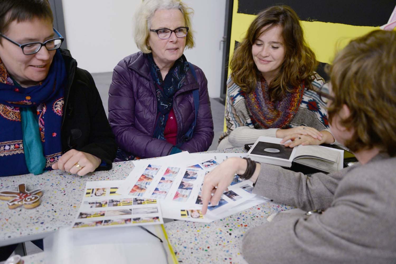 Vier Frauen sitzen um einen Tisch und betrachten Fotos, während eine von ihnen spricht.