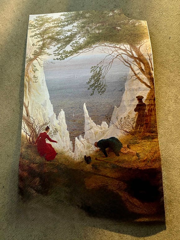 A scenic view featuring two figures, a woman in a red dress and a man in dark clothing, near a rocky cliff facing the sea, with natural foliage surrounding them.